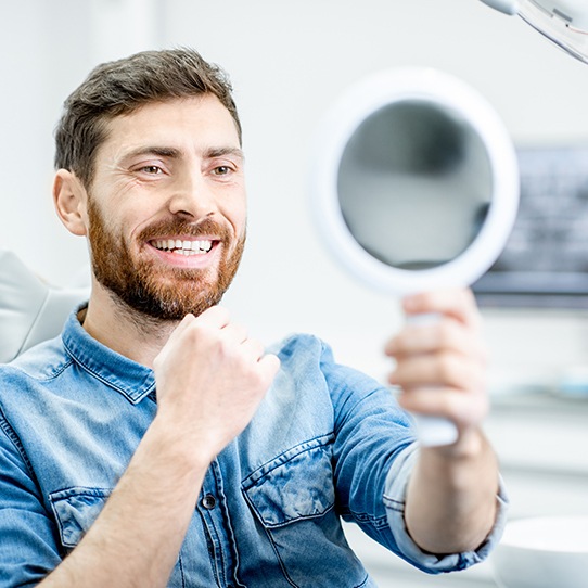 Man looking at smile in mirror during dental treatment