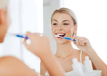 Woman brushing her teeth to prevent dental emergencies in Shelton