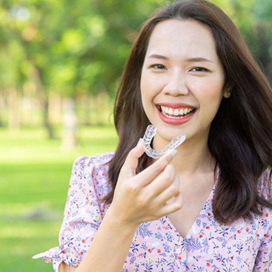 Smiling woman outside holding Invisalign in Shelton
